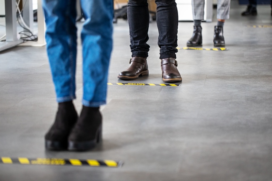 Low angle shot of business people standing behind social distancing signage on office floor. People in queue at office for safe entry checks post corona virus pandemic.