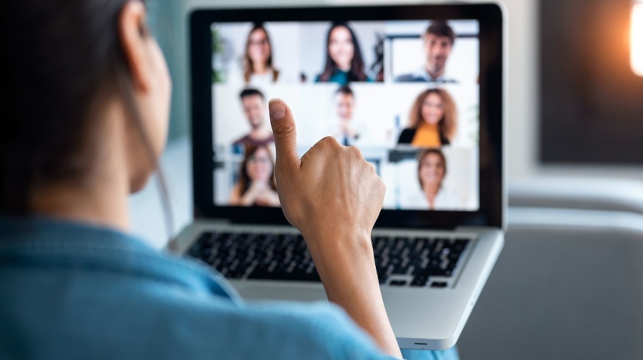 Back view of business woman making video call and showing thumb up to laptop on the online briefing while sit on sofa at home.