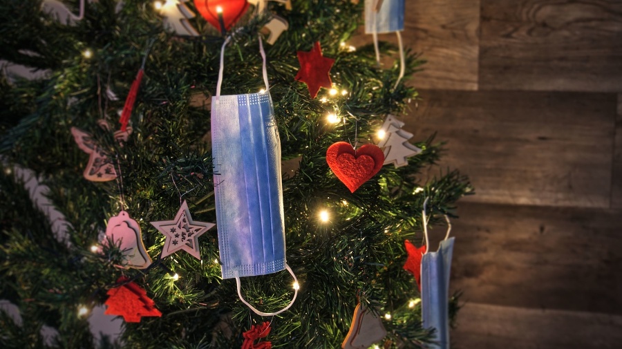 Christmas tree 2021 composition decorated with blue medical corona virus face masks and winter ornaments with sparkling lights on blurred wood background. Merry Christmas in covid-19 pandemic. Safe holiday celebration. Covid, new normal and happy new year concept.