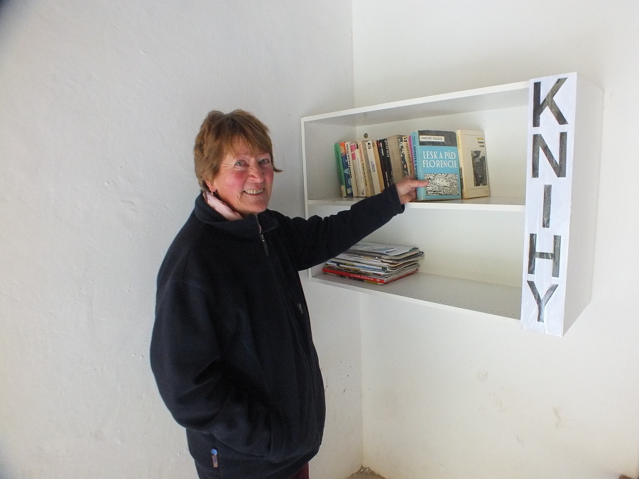 Dôchodkyňa Eva (76) na opravenej staničke Stratená, kde majú cestujúci k dispozícii na čítanie aj knihy.