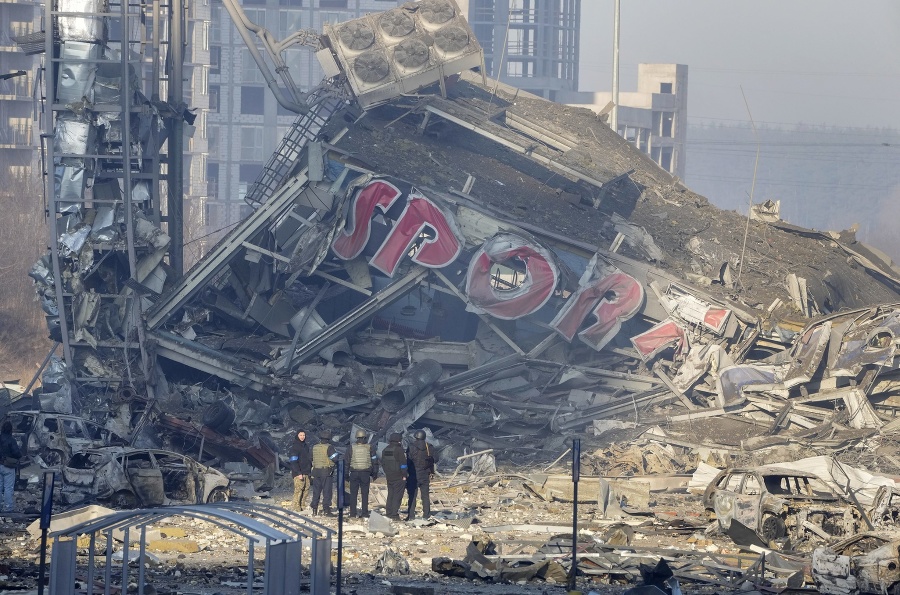Ľudia vyšetrujú škody zničeného obchodného centra po ruskom bomardovaní v Kyjeve 21. marca 2022. 