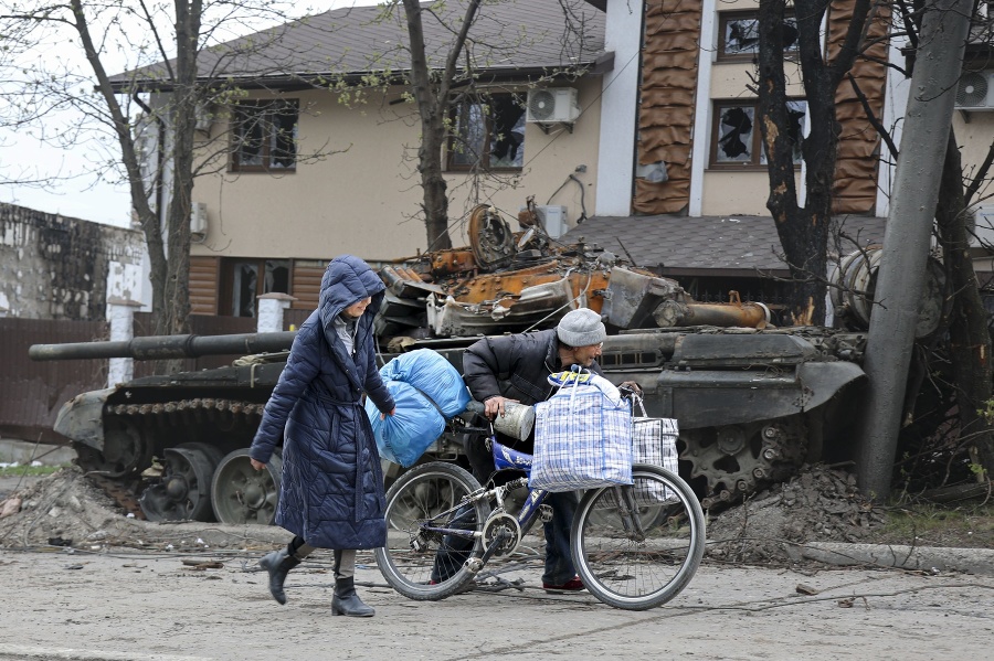 Miestni civilisti kráčajú okolo zničeného tanku počas bojov medzi ukrajinskou a ruskou armádou v obliehanom meste Mariupol.