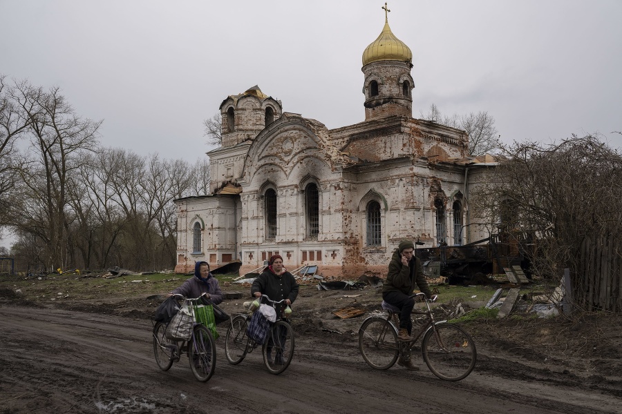 Obyvatelia s bicyklami pred poškodeným kostolom v Lukashivke na severe Ukrajiny v piatok 22. apríla 2022.