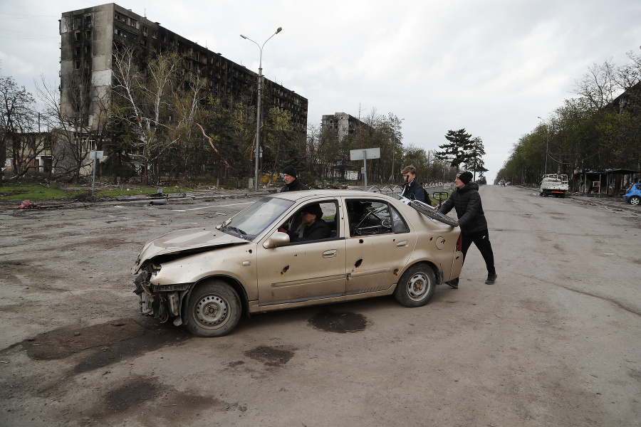Muži tlačia poškodené auto v Mariupoli.
