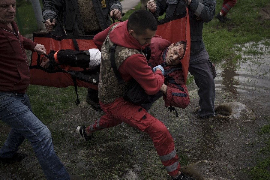 Záchranár a miestni ľudia odnášajú zraneného muža do sanitky po ruskom bombardovaní v meste Charkov.