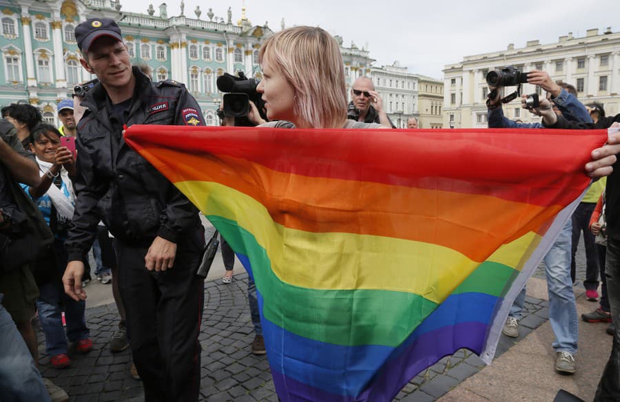 Policajt sa rozpráva s aktivistom za práva homosexuálov, ktorý stojí s dúhovou vlajkou pred novinármi počas protestnej akcie na Dvorcovom námestí v Petrohrade, Rusko, 2. augusta 2015.