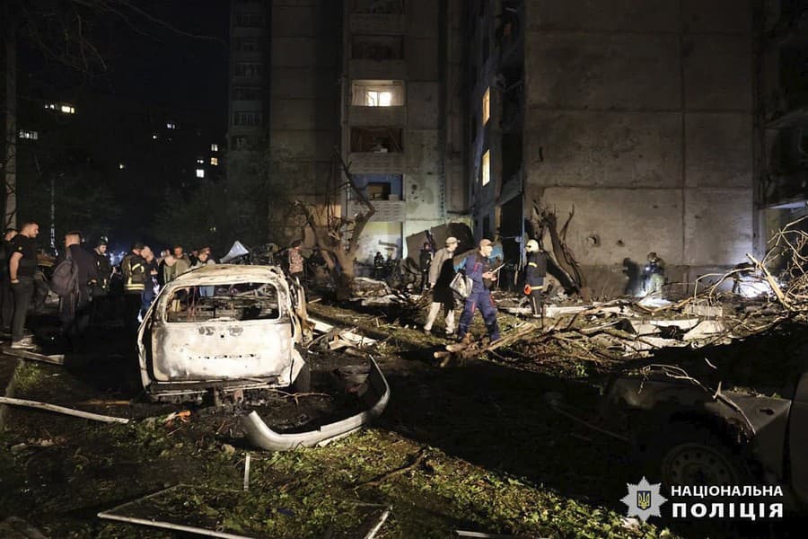 Ľudia stoja pri vrakoch áut po bombovom útoku ruskej armády na obytnú budovu v ukrajinskom meste Charkov v skorých ranných hodinách v nedeľu 22. septembra 2024.