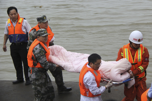 Záchranári nesú mŕtve telo pasažiera z lode, ktorá sa prevrátila na rieke Jang-c'-ťiang.