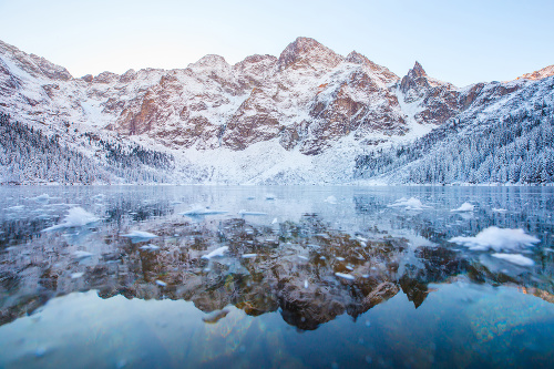 Mountains with reflection in lake. Winter morning landscape with snowy mountains and frozen lake. Selective focus. Blue winter colors. Christmas natural background. Winter scenic backdrop.