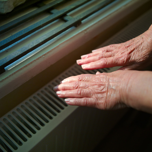Senior female hands near a central heater, indoor close-up, squzre composition