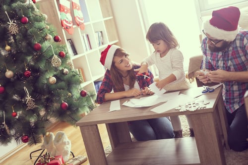 Mother, father and daughter sitting on a living room floor, cutting paper snowflakes and enjoying winter holidays together. Focus on the mother