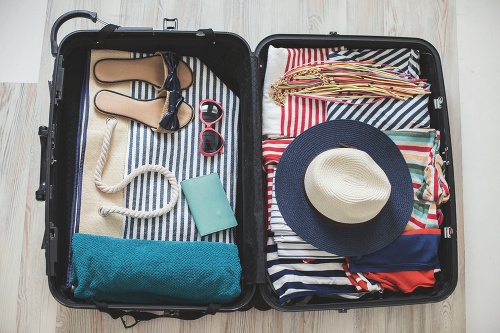 High angle view of summer clothes, slippers, sun hat, sun glasses, beach towel, and other accessories arranged in a suitcase.
