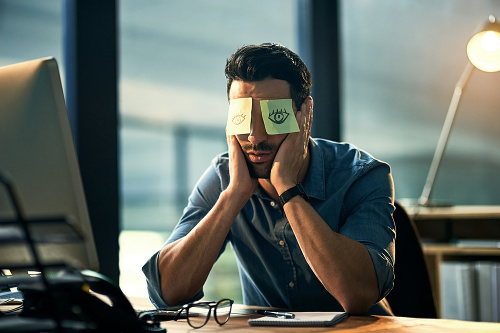 Shot of a tired young businessman working late in an office with adhesive notes covering his eyes