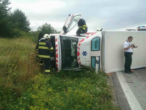 Sanitka po zráže s osobným autom ostala prevrátená na boku.