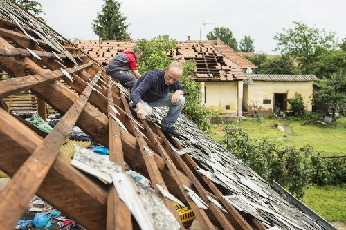  Na snímke zľava István Nagy a Aron István Nagy odstraňuje poškodené škridly zo strechy domu po silnom krupobytí v dedine Rozsály.