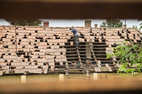 Na snímke muž odstraňuje poškodené škridly zo strechy domu po silnom krupobytí v dedine Rozsály.