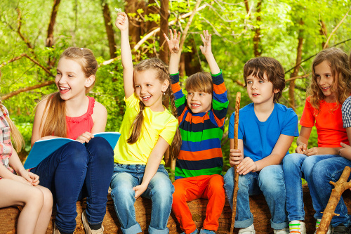 Portrait of happy boys and girls having fun, sitting in a row on the log, in the summer camp