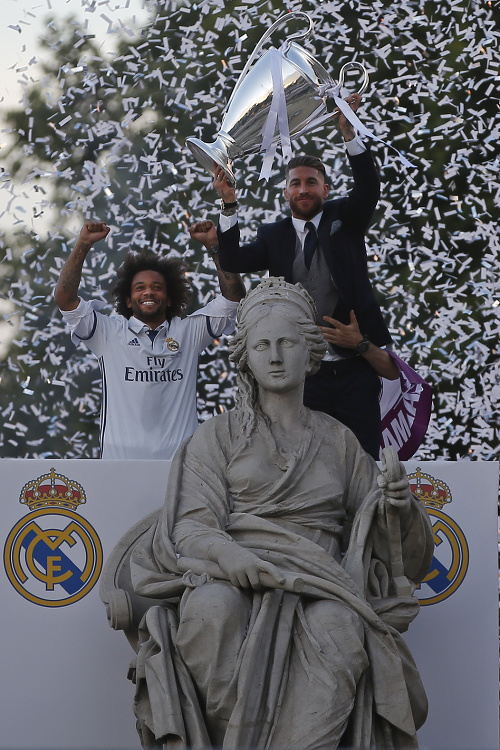 Futbalisti Realu Madrid Sergio Ramos (vpravo) a Marcelo dvíhajú pohárovú trofej nad hlavu pri soche Cibeles. 