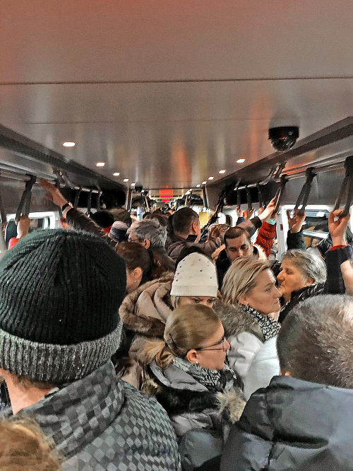 Ľudia cestujú do práce v preplnených vlakoch.