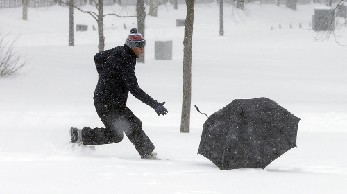 Muž uteká za odfúknutým dáždnikom počas silnej snehovej búrky v Bostone.