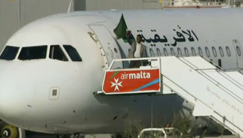 Nezmámy muž máva vlajkou na schodoch uneseného lietadla líbyjskej spoločnosti Afriqiyah Airways.