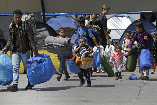 Migranti nesú svoje veci pri pobreží Egejského mora v prístave v meste Piraeus pri Aténach.