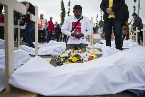 Aktivisti ležia zabalení v bielych plachtách pri drevených krížov na proteste s názvom 
