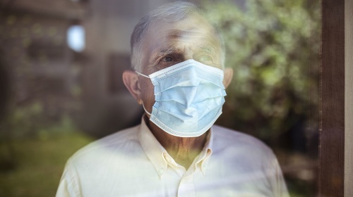 Senior man stays home because of Corona virus. He stands by the window and looks out at the garden.