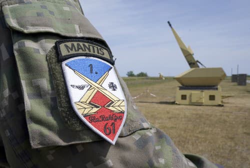 Znak protilietadlovej raketovej skupiny 61 Luftwaffe vidieť na rukáve vojaka vedľa zbraňového systému protivzdušnej obrany Mantis