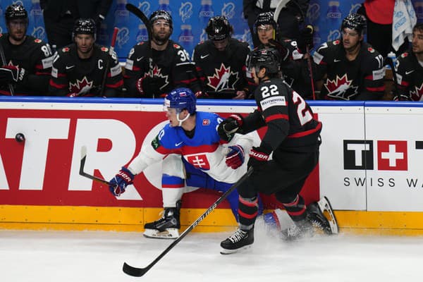 Slovenský hokejista Juraj Slafkovský (vľavo) a hráč Kanady Dylan Cozens bojujú o puk pri mantineli.