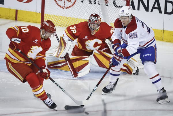 Christian Dvorak z Montreal Canadiens (vpravo) a Jonathan Huberdeau z Calgary Flames (vľavo) bojujú o puk, zatiaľ čo brankár Dustin Wolf sleduje hru.