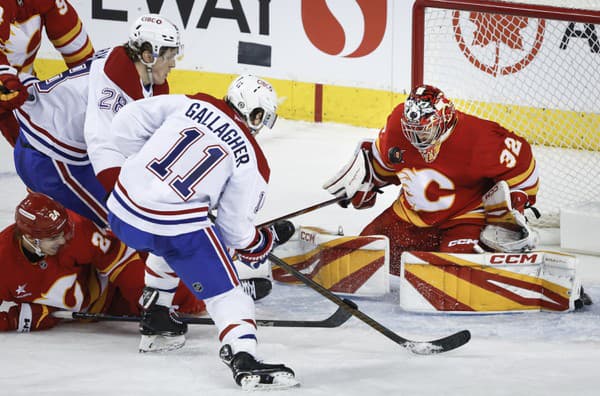 Christian Dvorak (28) a Brendan Gallagher (11) z Montreal Canadiens sledujú hru, zatiaľ čo brankár Calgary Flames Dustin Wolf (vpravo) bráni svoju bránku